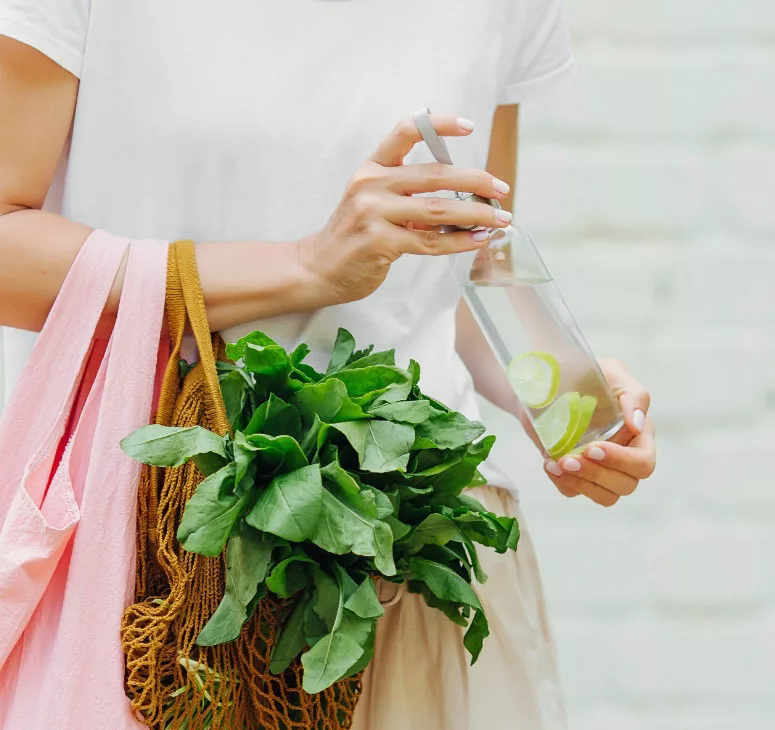 A woman holding a pink bag and a water bottle filled with water and sliced lemon.