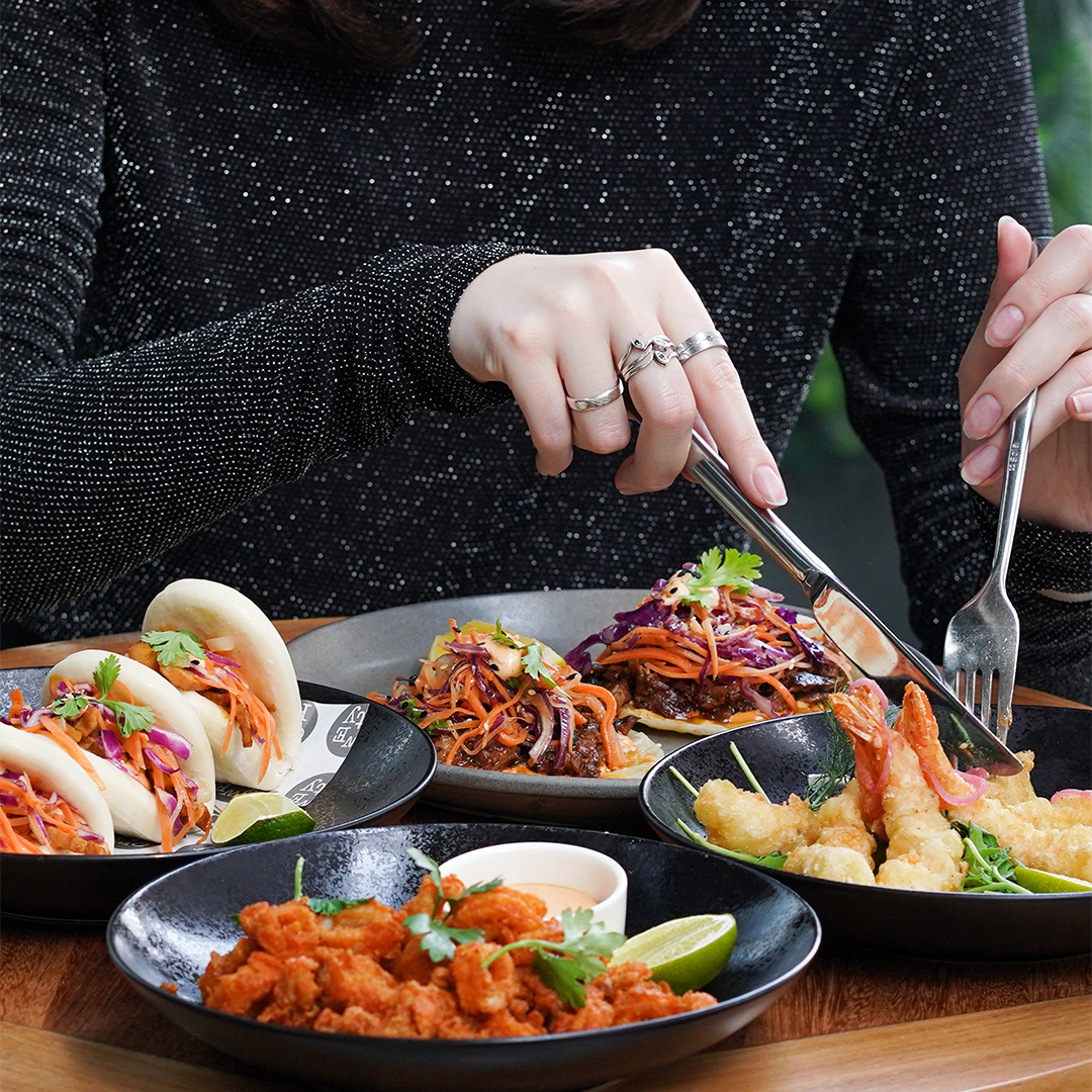 A woman enjoying several dishes using a knife and fork.