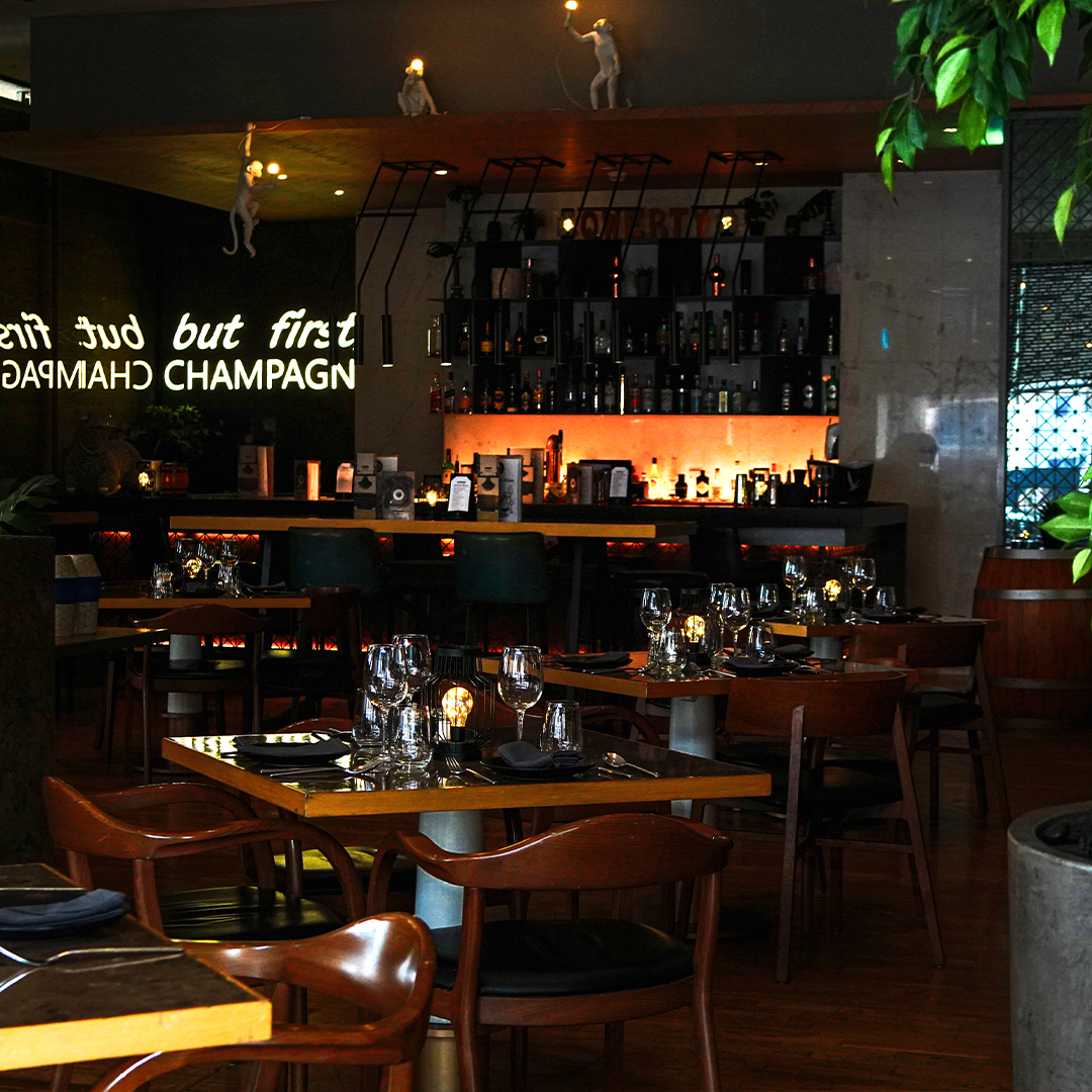 Inside of a bar with tables, chairs, wine glasses and the bar in the distance.