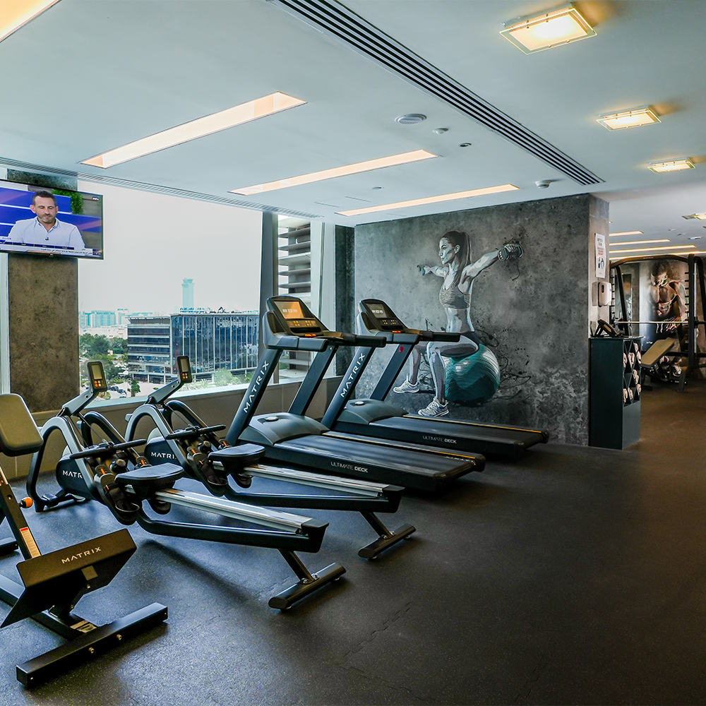 Media One Hotel gym with rowing machines, treadmills and a window showing the city.