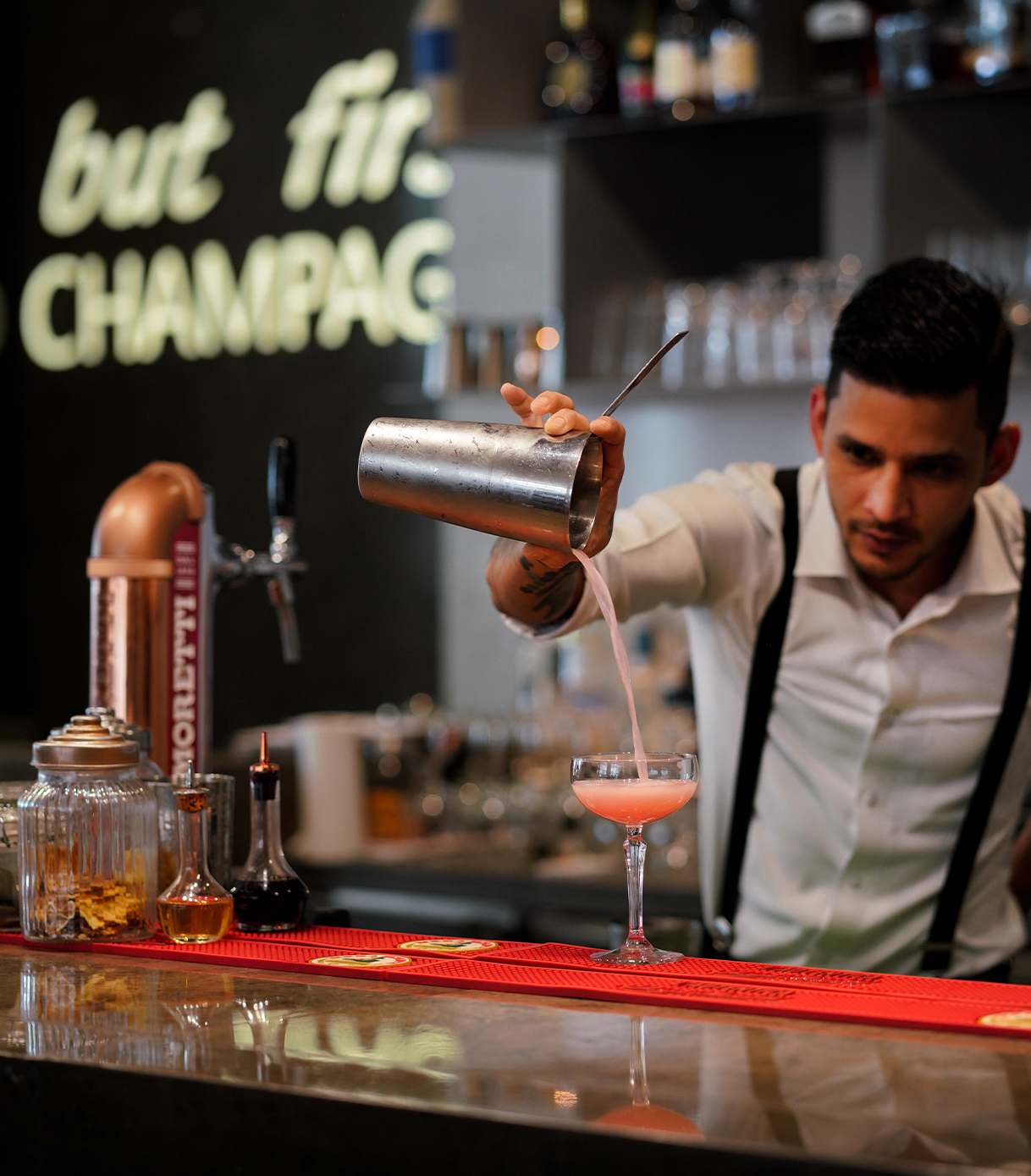 A mixologist preparing a pink cocktail on the bar.