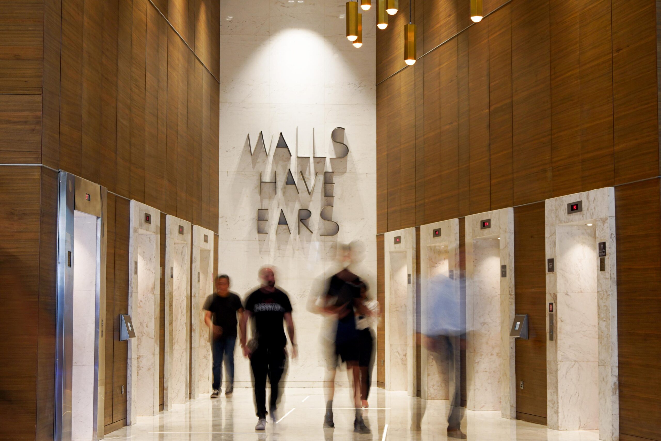 Elevators at the bottom of the office tower building with people walking through.