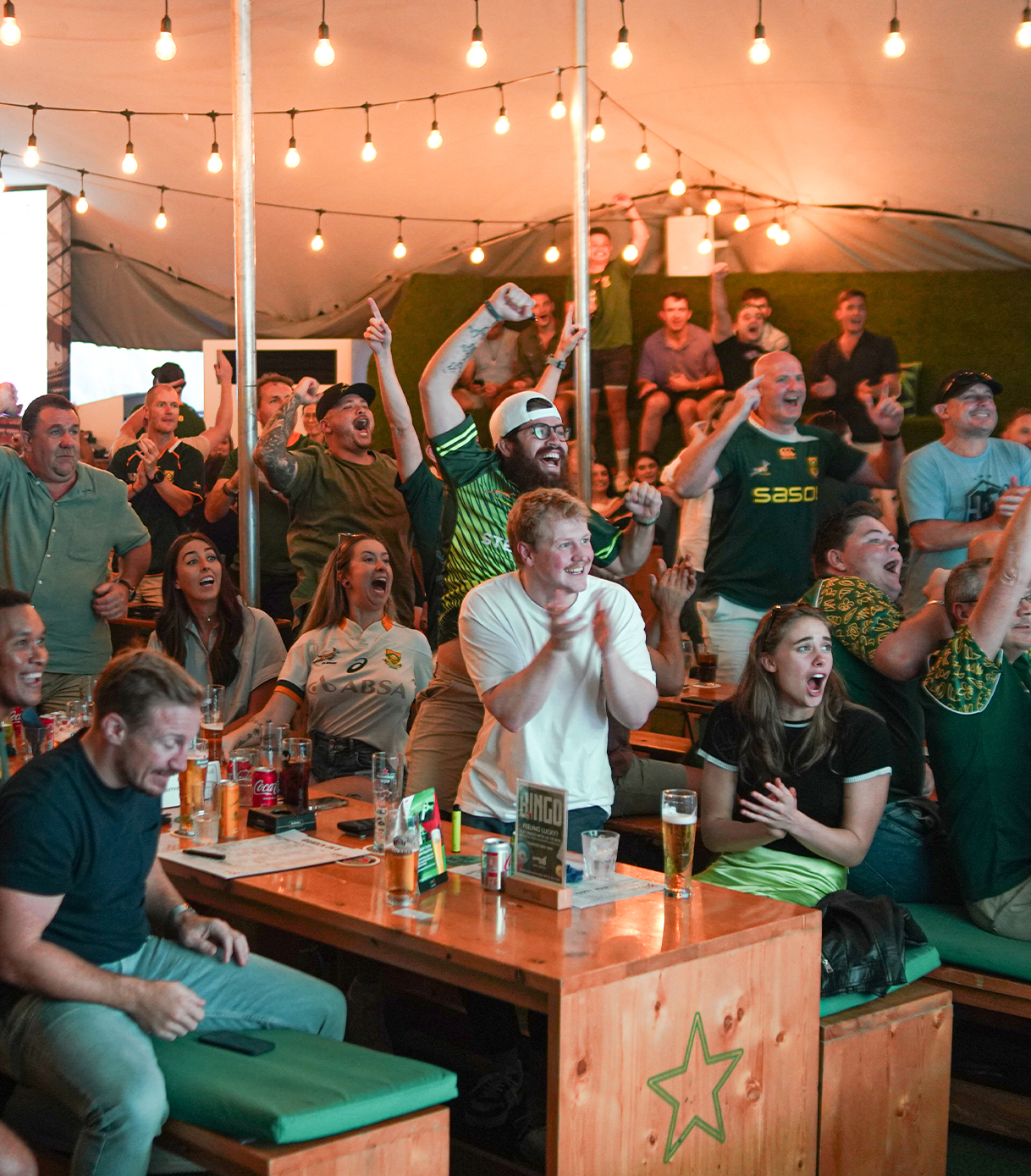 A beer garden with fans cheering on their sports team around their tables.