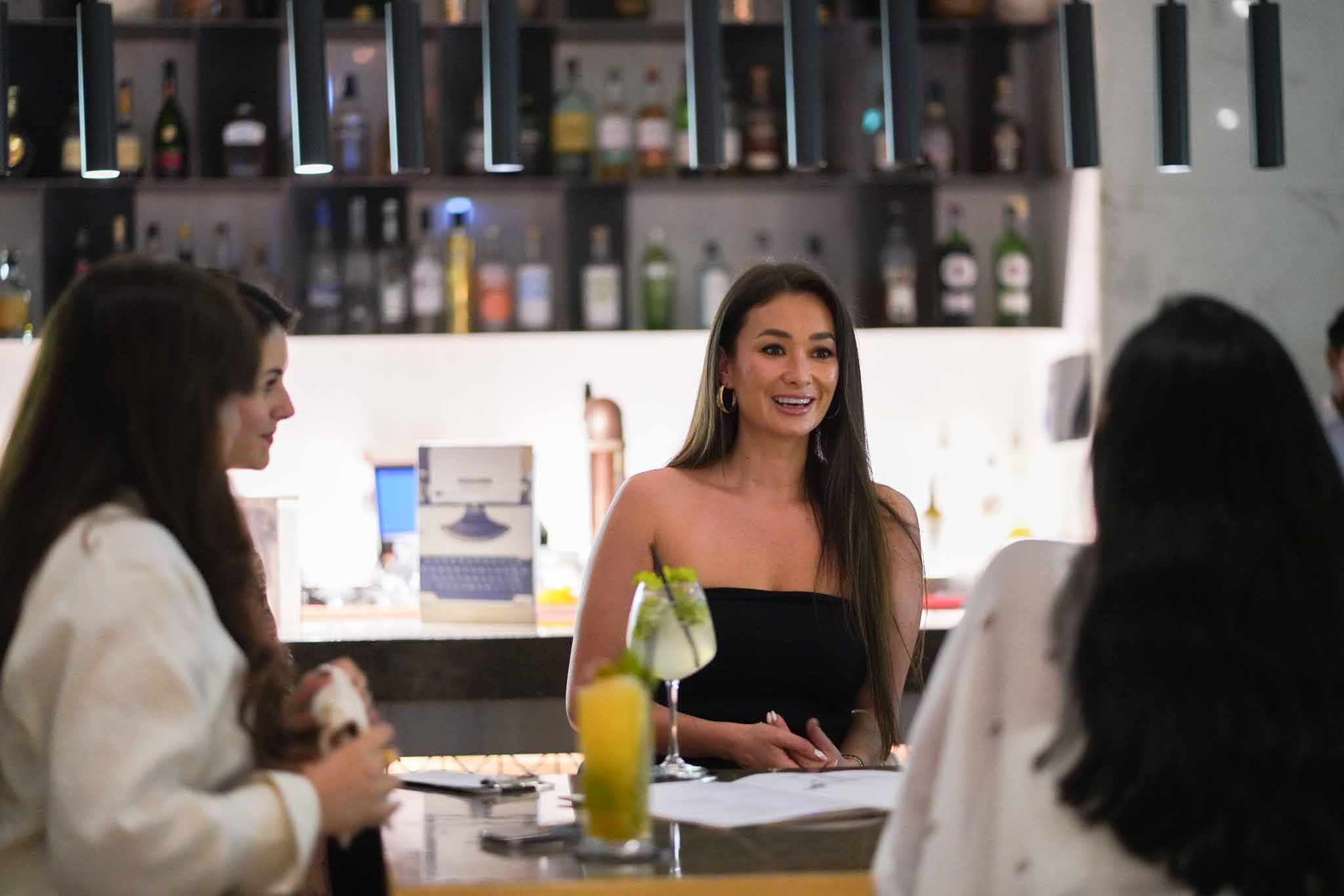 Two men leaning on a bar smiling at each other waiting to be served a drink.